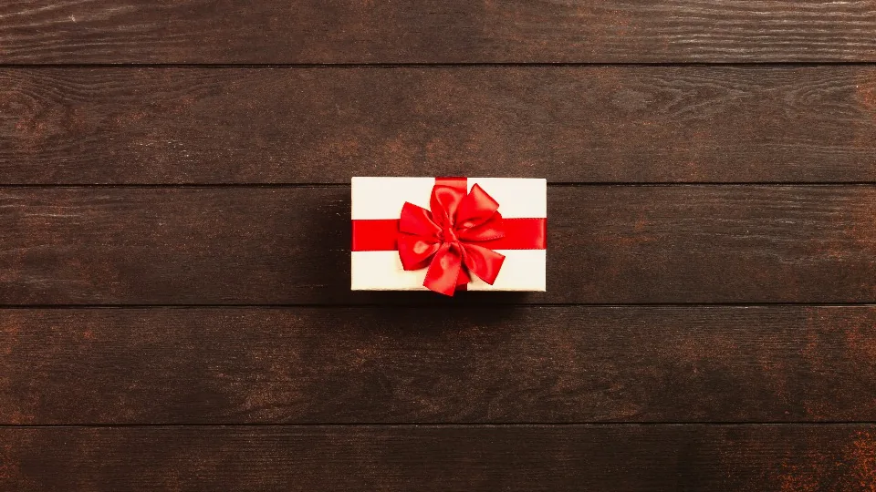A small gift box with a red ribbon on a dark wooden table - P2P welcome bonuses